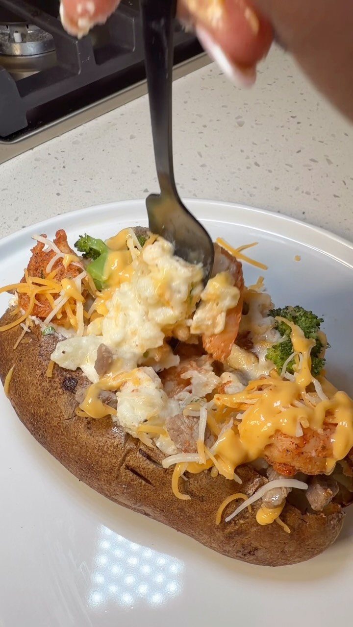 Loaded baked potato with melted cheese and broccoli on a white plate.