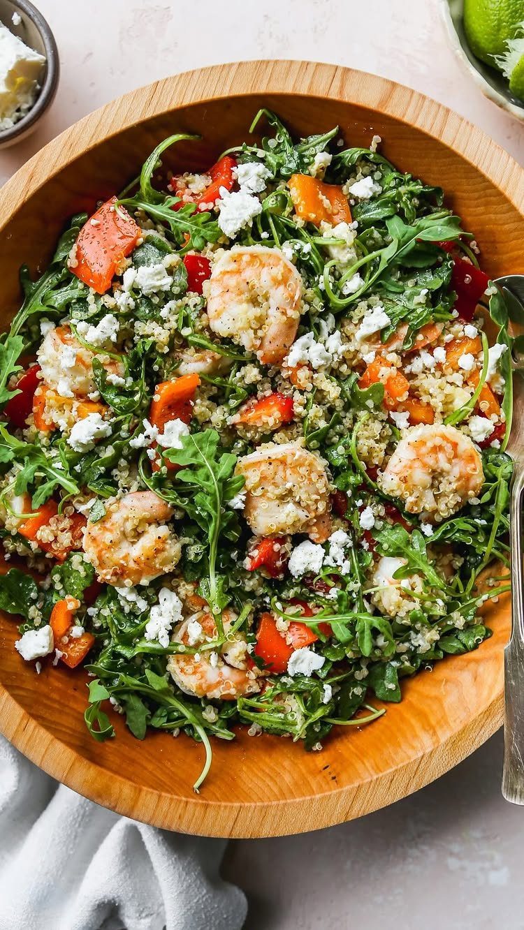Quinoa shrimp salad with red bell peppers, feta cheese, and arugula in a wooden bowl