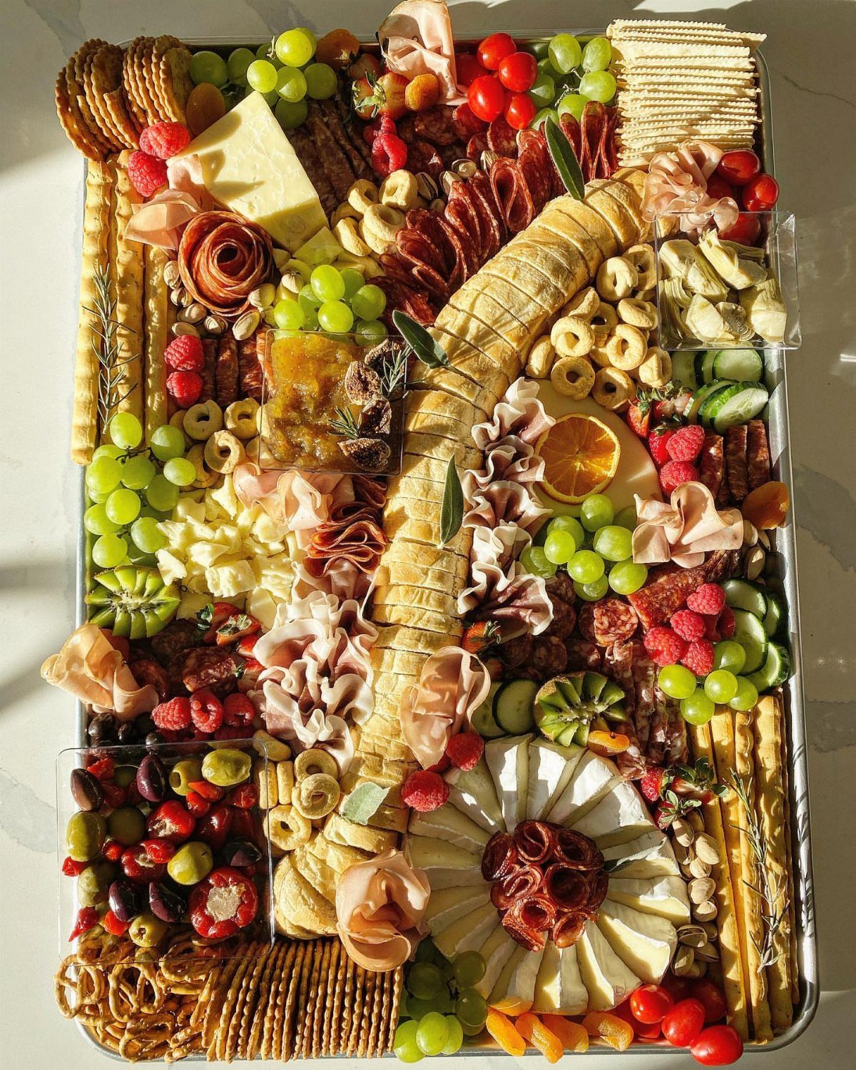 Large charcuterie board with assorted meats, cheeses, fruits, and crackers in a dense arrangement.