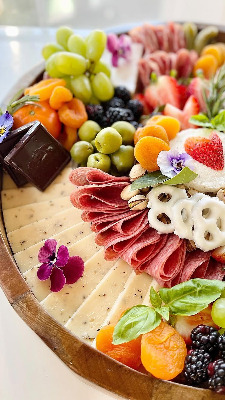 Charcuterie board with green olives, salami, cheese, fresh fruits, and edible flowers.