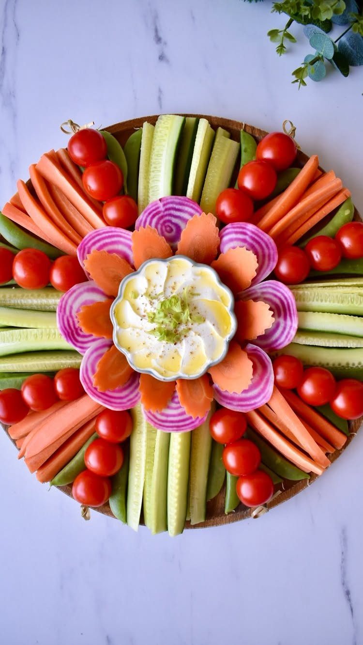 Vegetable platter with carrots, cucumbers, radishes, and cherry tomatoes surrounding a central dip bowl.