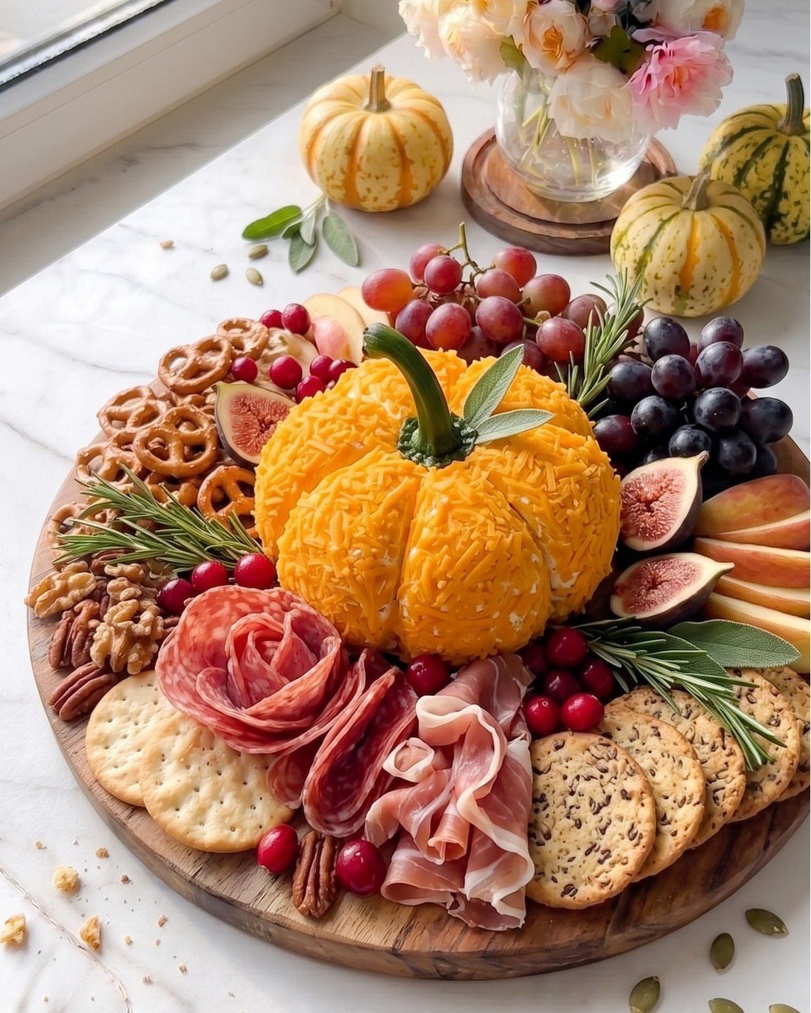 Pumpkin-shaped cheddar cheese centerpiece on a charcuterie board with meats, fruits, and crackers.