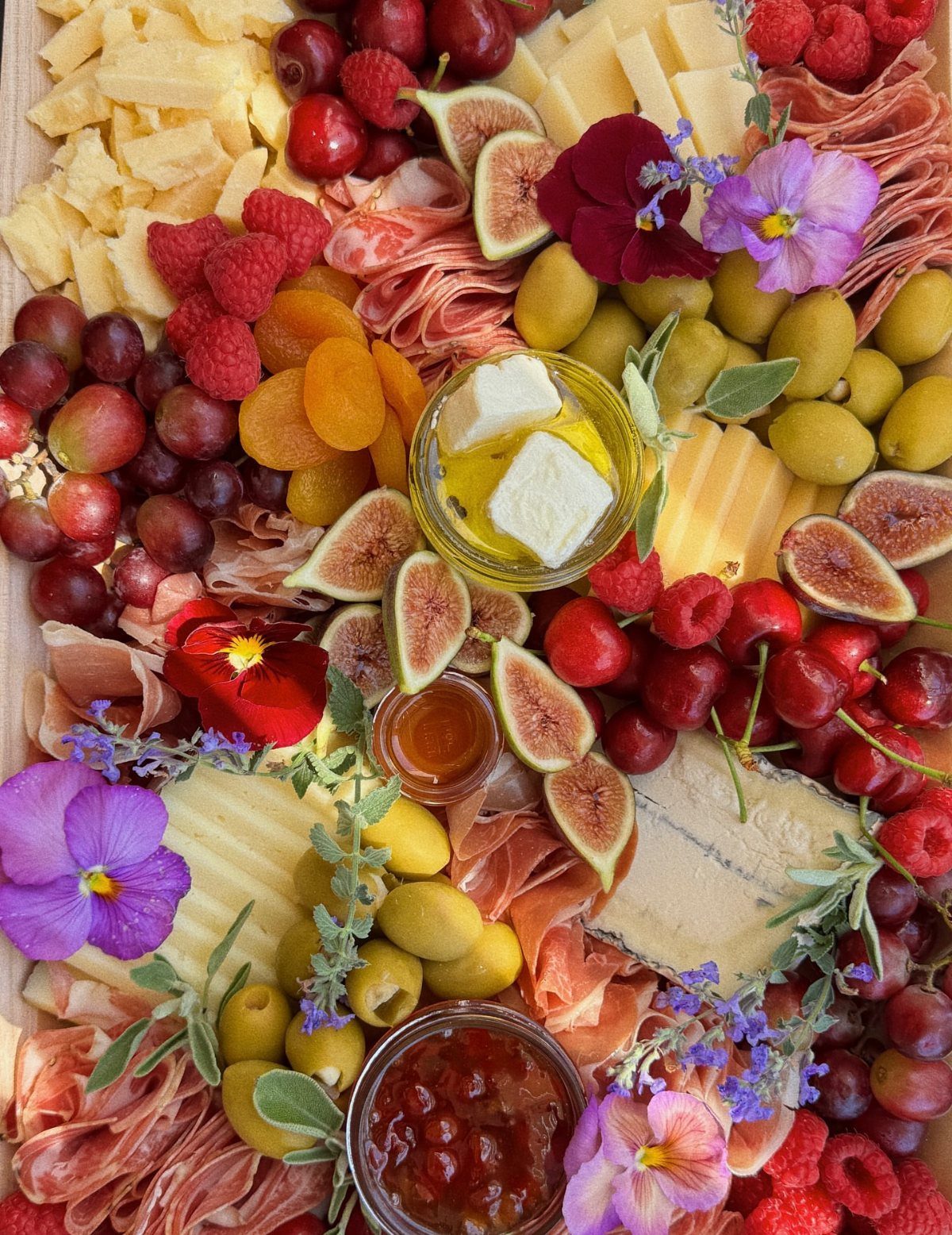 Charcuterie board with assorted cheeses, meats, fresh fruits, olives, and colorful edible flowers.
