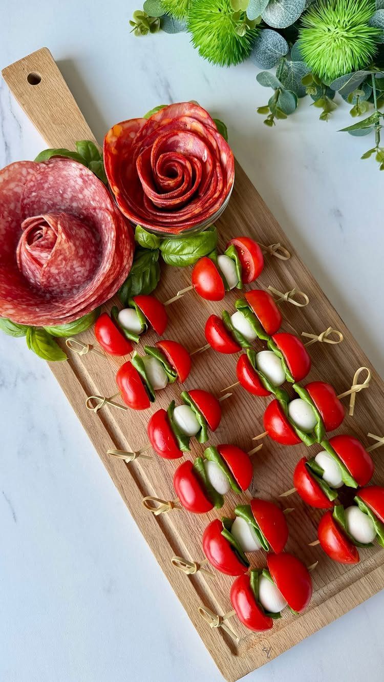 Caprese skewers and salami roses arranged on a wooden board over white marble.