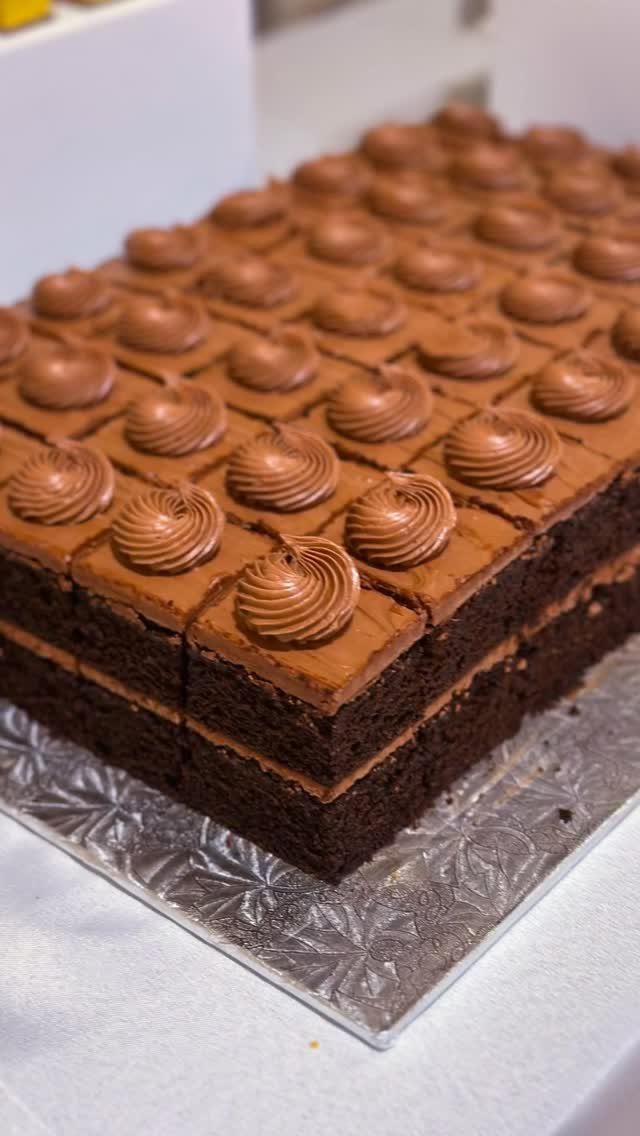 Chocolate sheet cake cut into squares with frosting swirls on a silver platter.