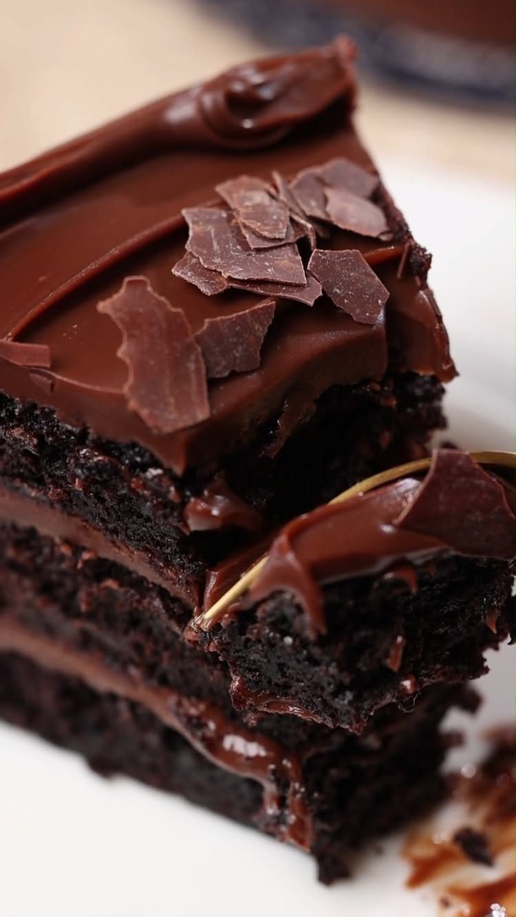 Slice of fudgy chocolate layer cake with thick frosting and chocolate shavings.