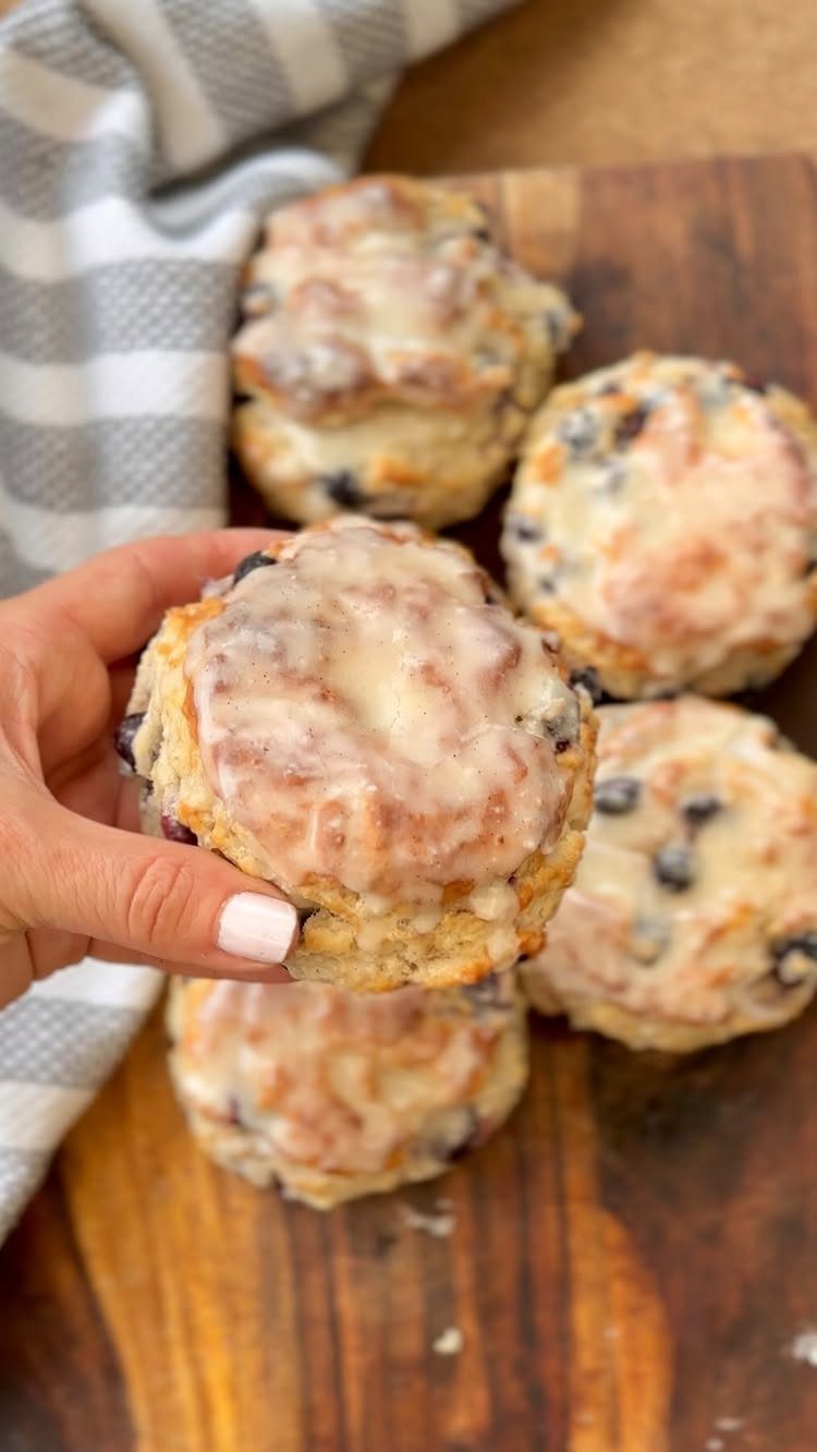 24 Desserts to Make with Blueberries, Cobbler to Cheesecake 17 Glazed blueberry biscuits on a wooden board with a hand holding one biscuit.