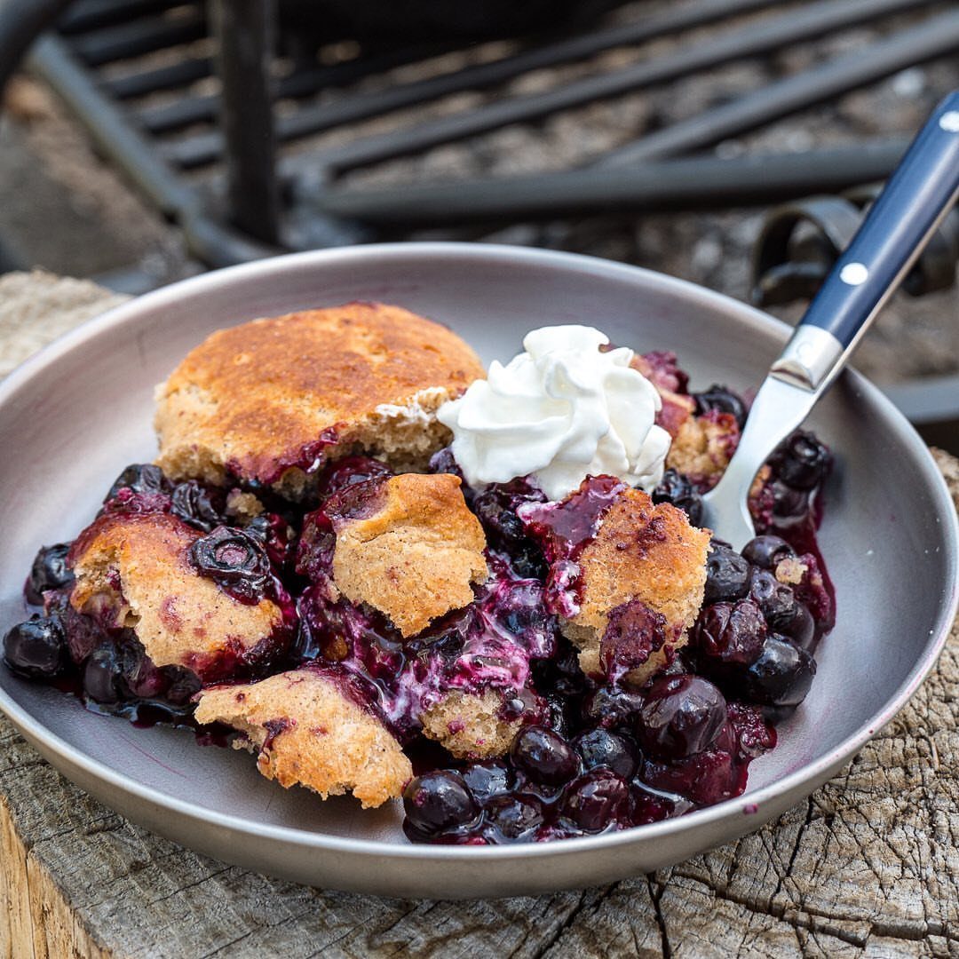 24 Desserts to Make with Blueberries, Cobbler to Cheesecake 11 Blueberry cobbler with biscuit topping and whipped cream in a silver baking pan.