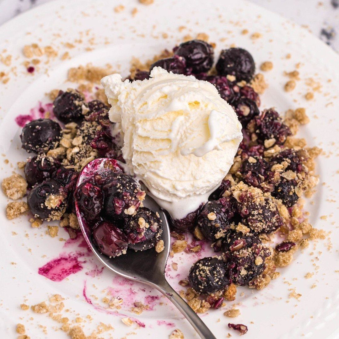 24 Desserts to Make with Blueberries, Cobbler to Cheesecake 4 Blueberry crumble with a scoop of vanilla ice cream on a white plate.