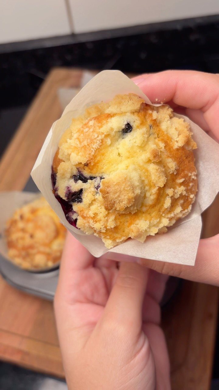 24 Desserts to Make with Blueberries, Cobbler to Cheesecake 2 Blueberry muffin with streusel topping held in hands wrapped in parchment paper.