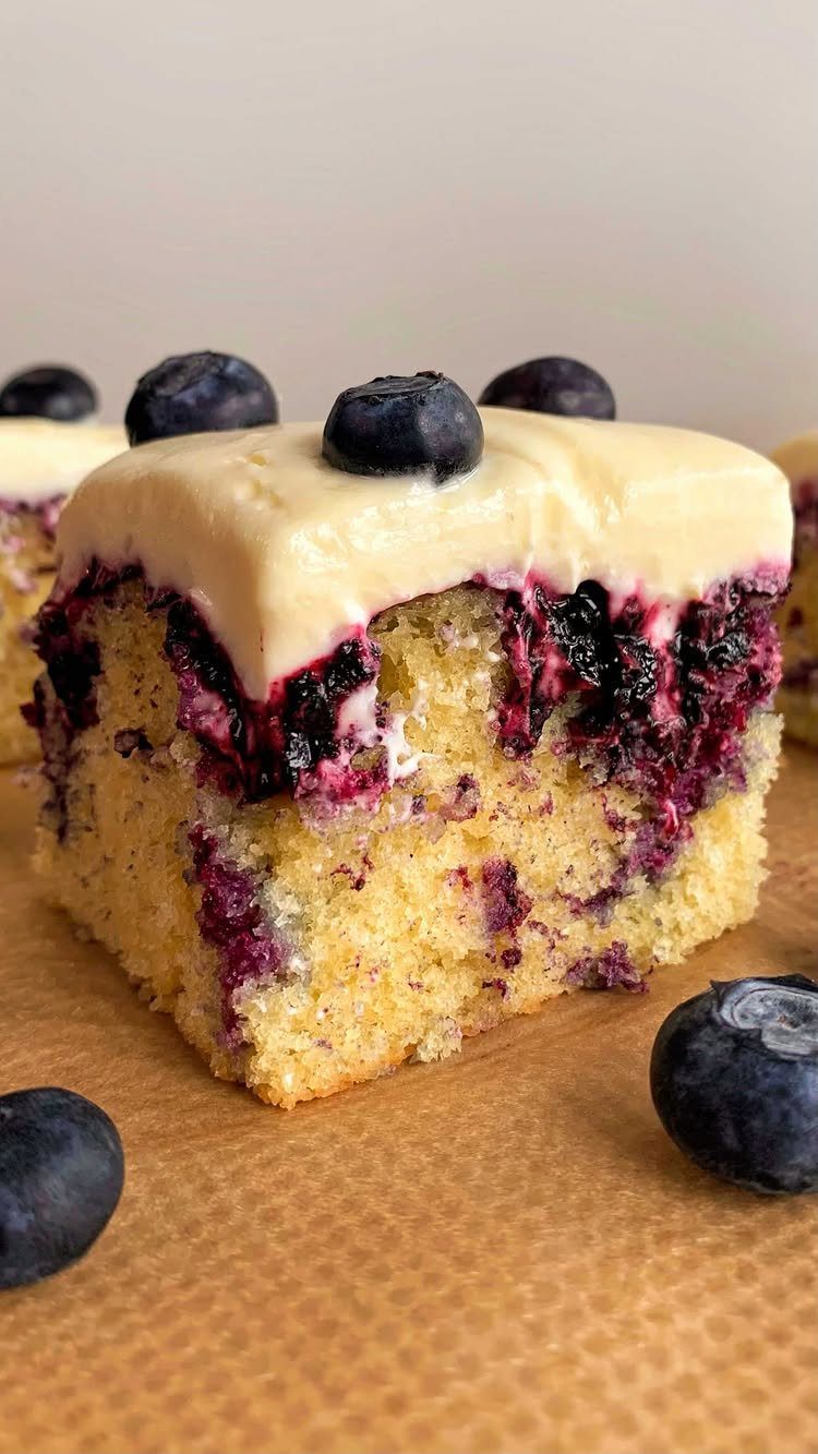 24 Desserts to Make with Blueberries, Cobbler to Cheesecake 21 Slice of blueberry poke cake with creamy frosting and fresh blueberries on top.