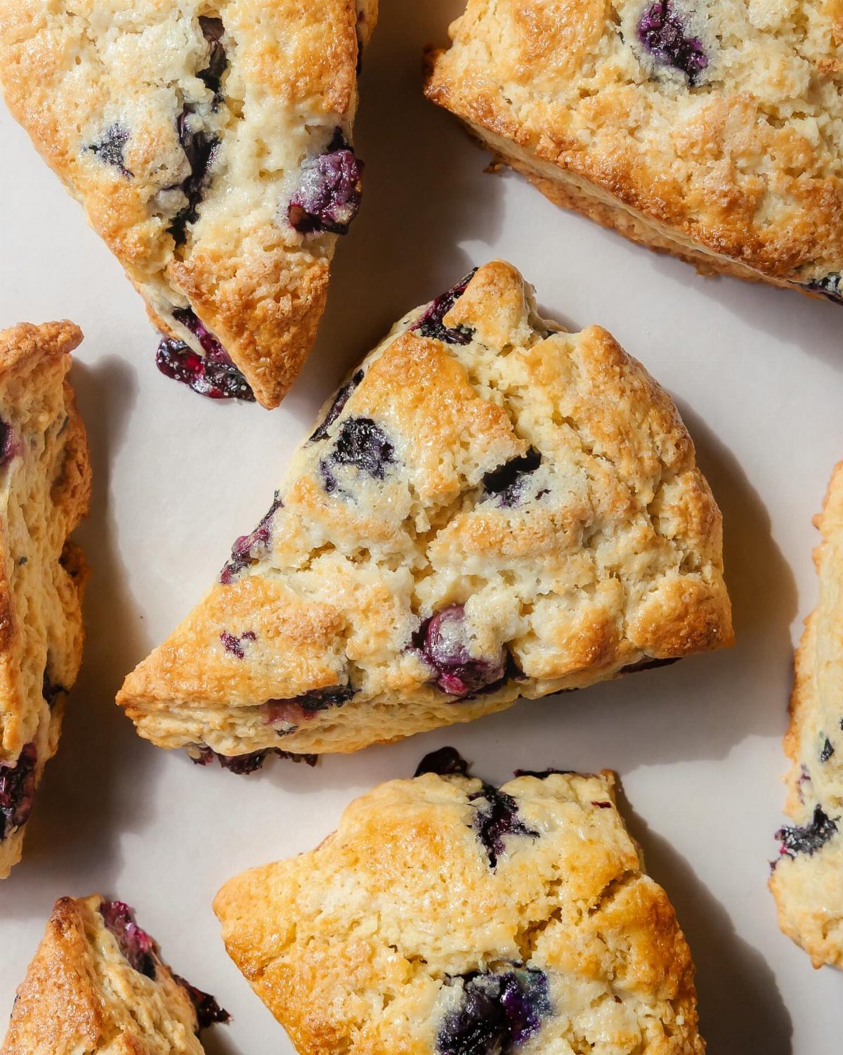 24 Desserts to Make with Blueberries, Cobbler to Cheesecake 15 Golden brown triangular blueberry scones with whole berries on white parchment paper.