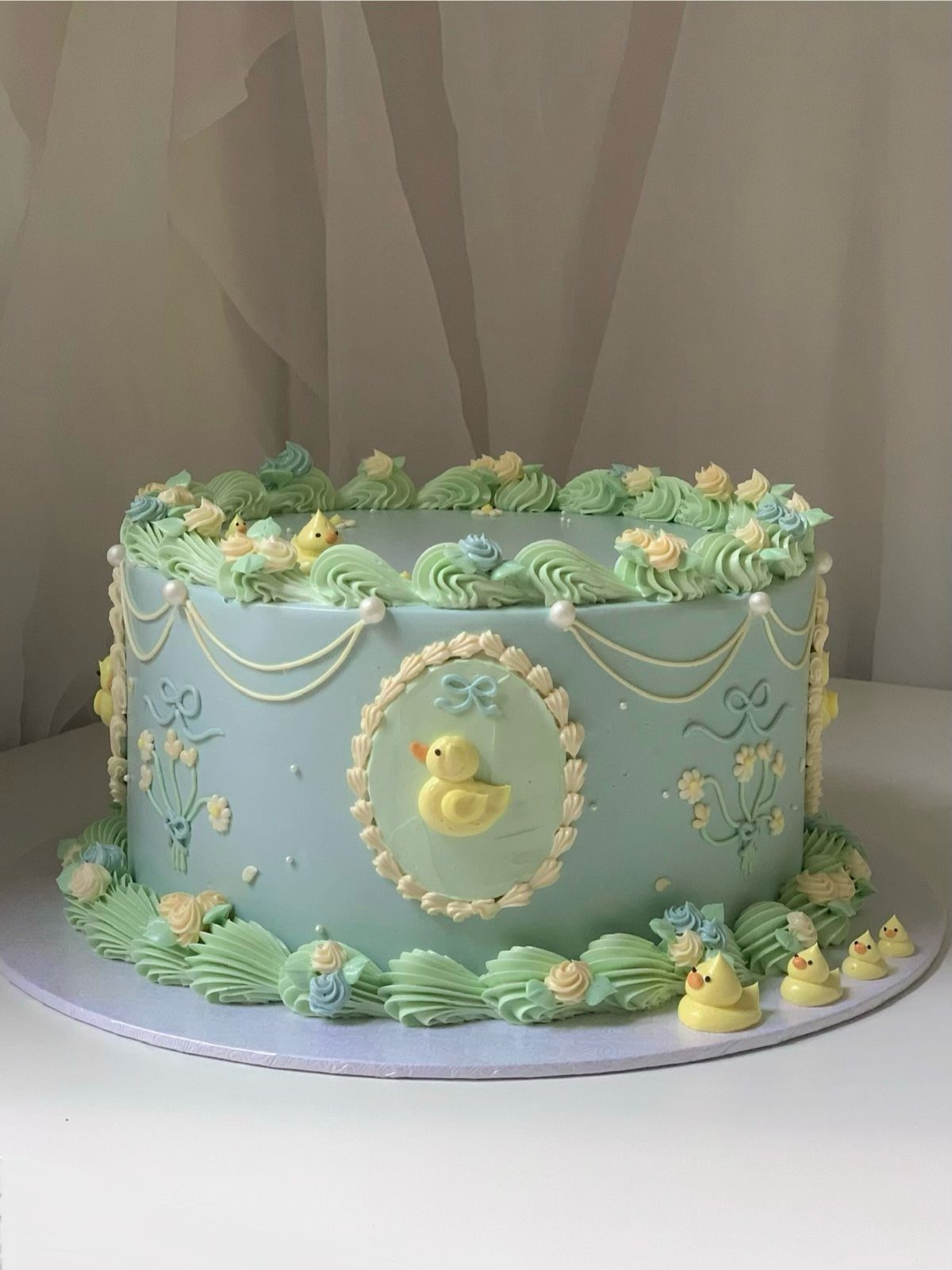 12 Duck Cakes Ideas for Birthdays, From Buttercream to Giant 5 Light blue cake with green frosting swirls and small yellow edible ducks.
