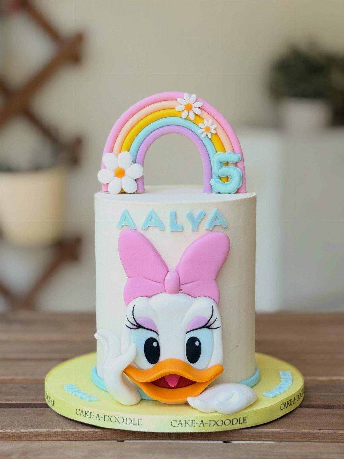 12 Duck Cakes Ideas for Birthdays, From Buttercream to Giant 9 Daisy Duck birthday cake with a colorful rainbow topper and pink bow detail.