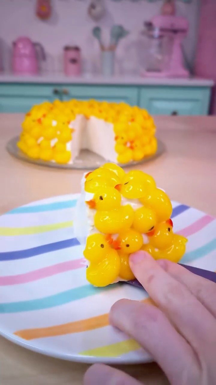 12 Duck Cakes Ideas for Birthdays, From Buttercream to Giant 4 White frosted cake covered in small yellow gelatin ducks on a striped plate.