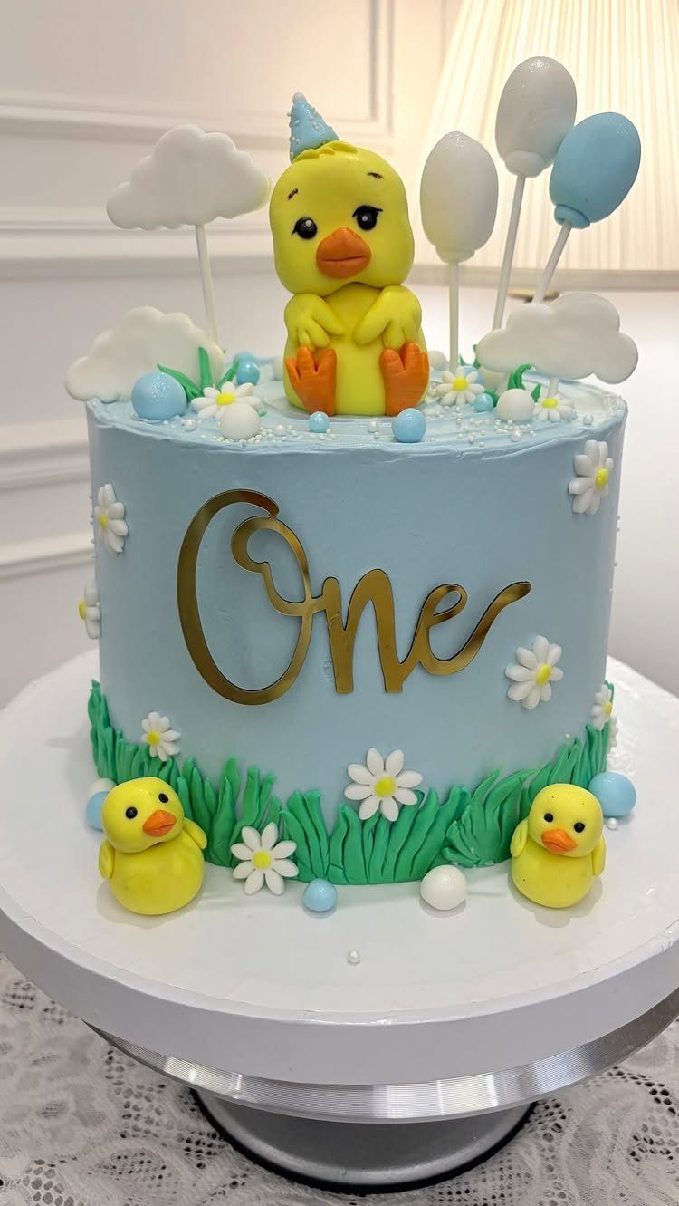 12 Duck Cakes Ideas for Birthdays, From Buttercream to Giant 12 Light blue birthday cake with yellow ducks, white daisies, and a gold One topper.