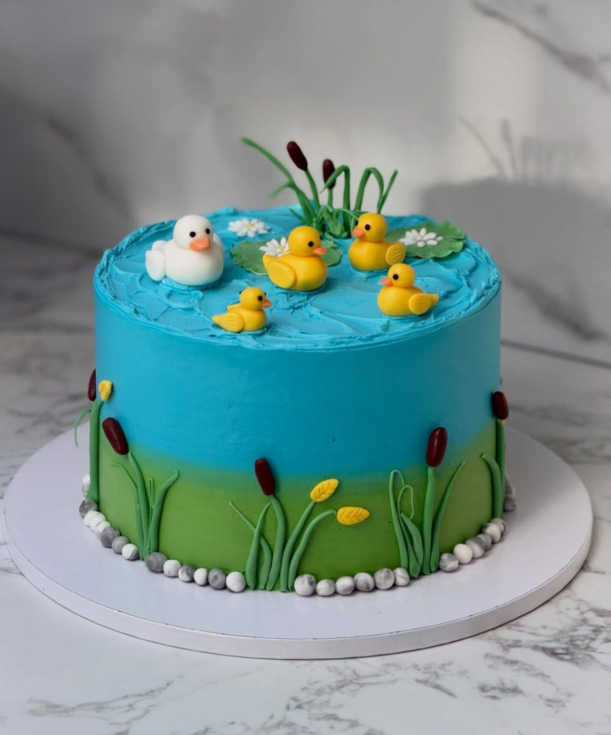 12 Duck Cakes Ideas for Birthdays, From Buttercream to Giant 6 Duck pond cake with blue water frosting, green grass, and small rubber ducks.