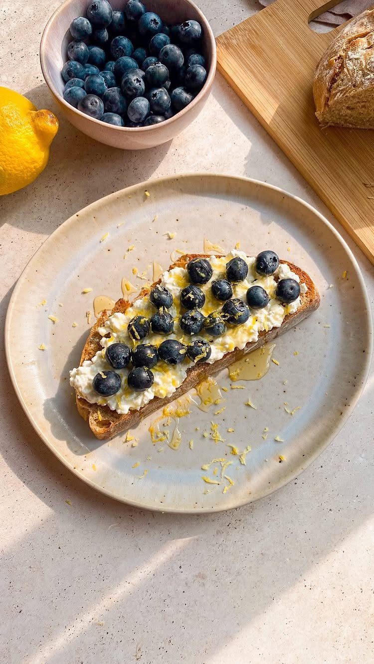 Toasted bread with cream cheese, blueberries, and lemon zest on a beige plate.