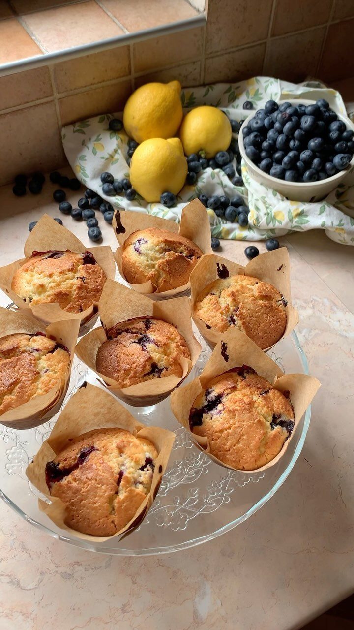 Blueberry muffins on a glass plate with fresh blueberries and lemons in background