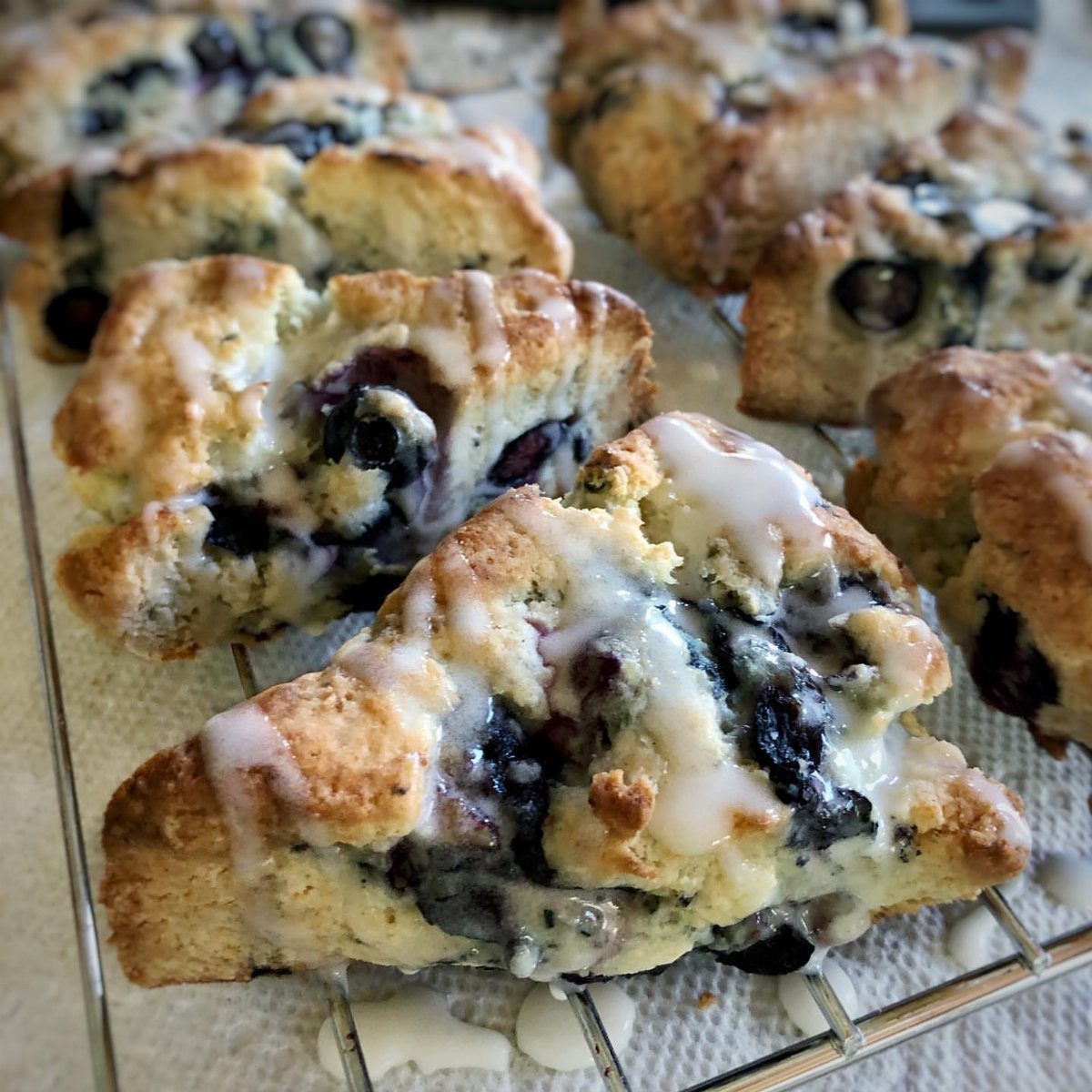 Blueberry scones with white vanilla icing drizzled on top on a wire cooling rack