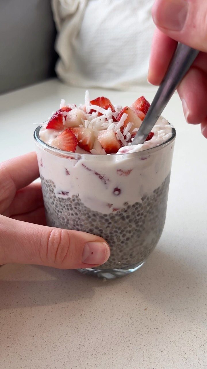 Chia seed pudding topped with strawberries and shredded coconut in a glass cup.