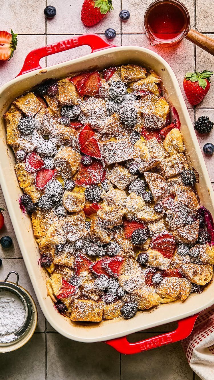 Baked French toast with strawberries and blackberries in a red ceramic baking dish.