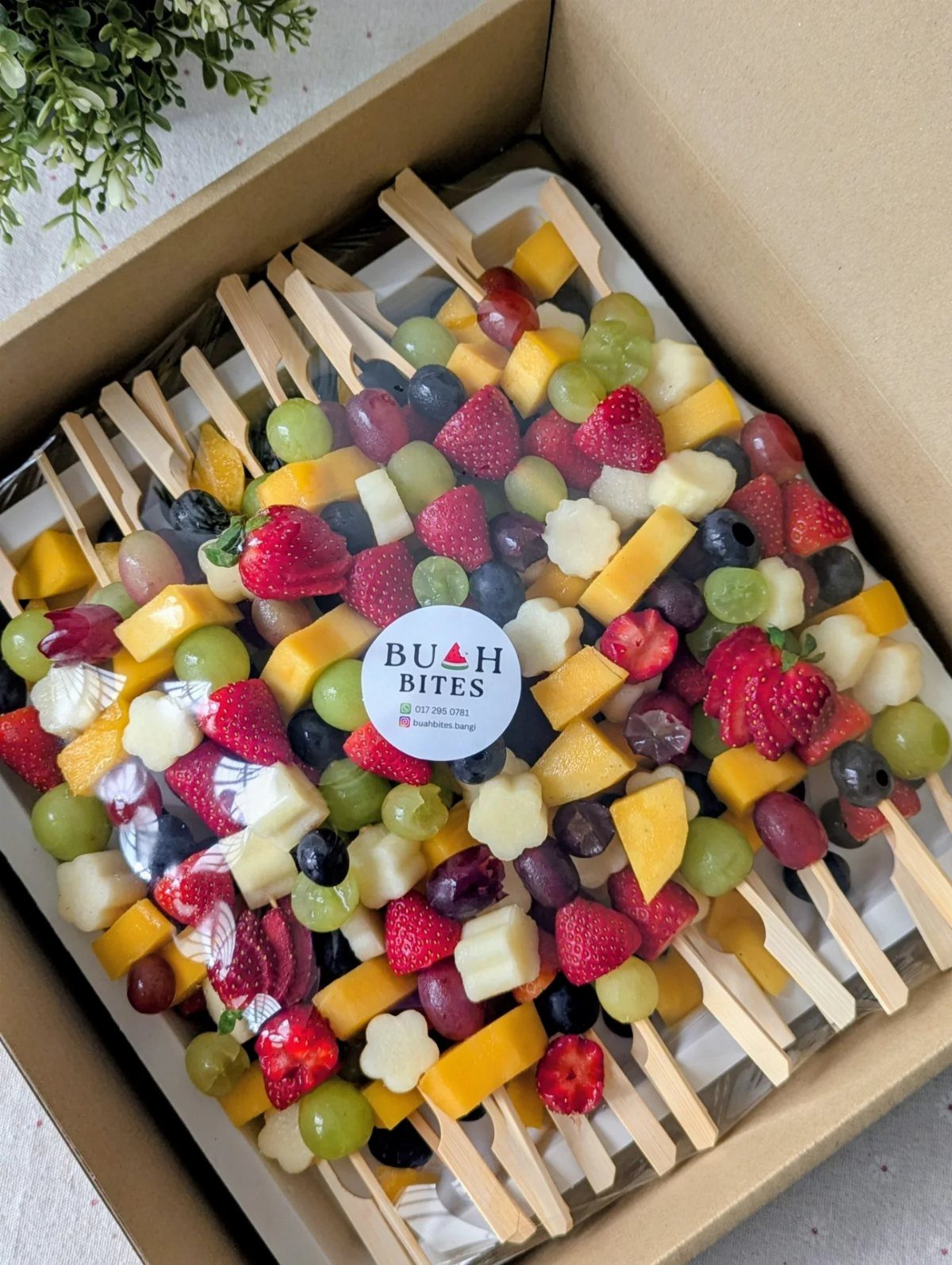 Fruit breakfast skewers with strawberries, grapes, and mango in a cardboard box.