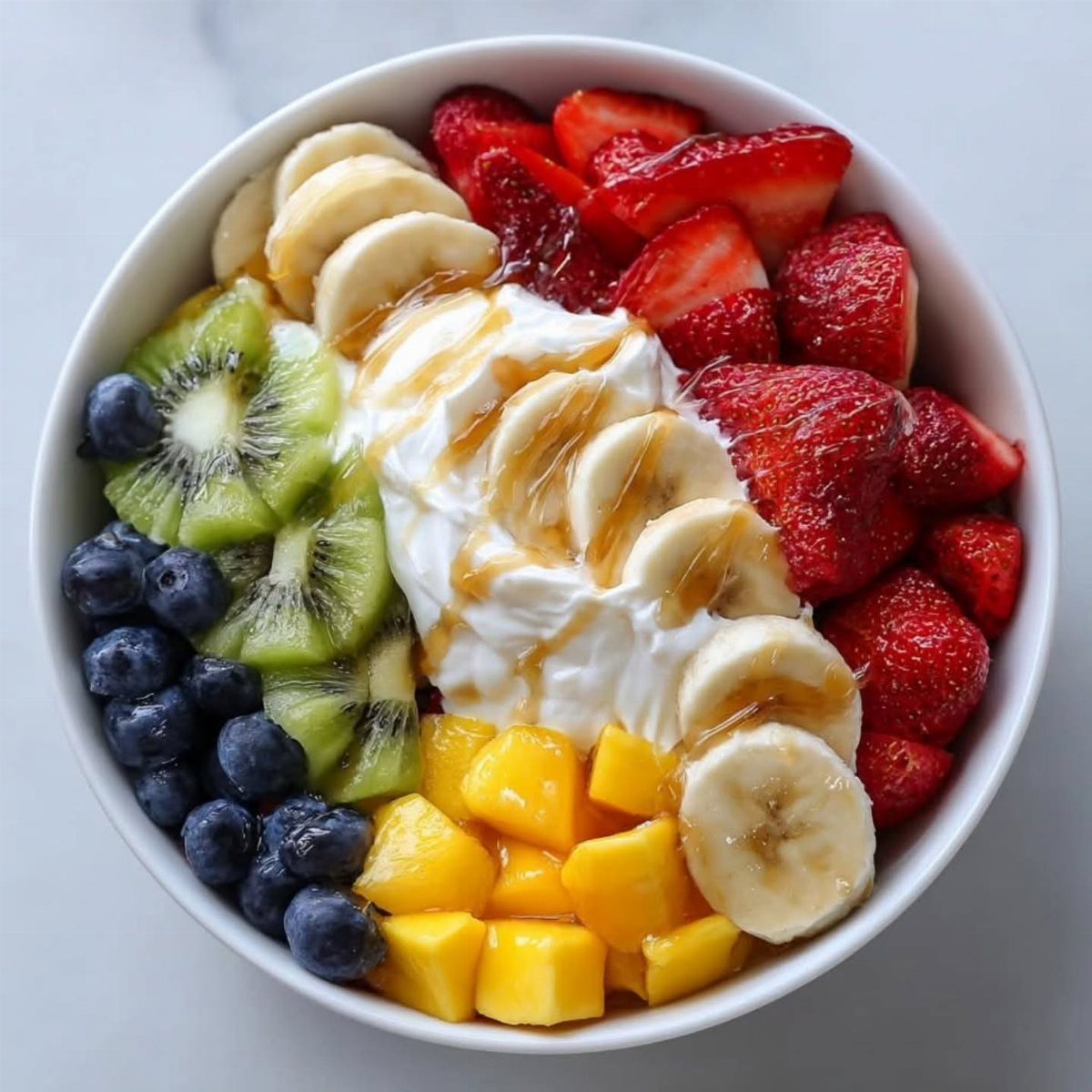 Fruit salad bowl with strawberries, blueberries, kiwi, mango, and yogurt drizzled with honey.