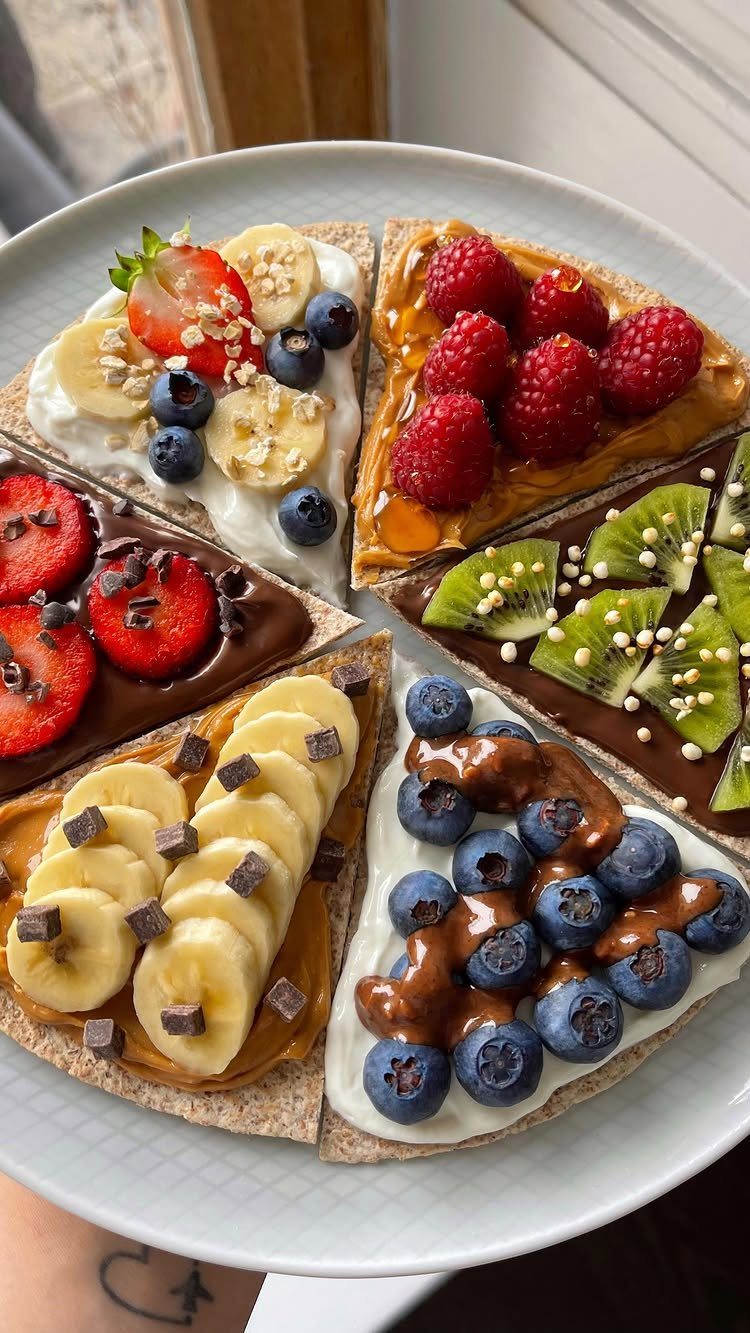 Five crispbread triangles topped with yogurt, nut butter, and various fresh berries and fruits.