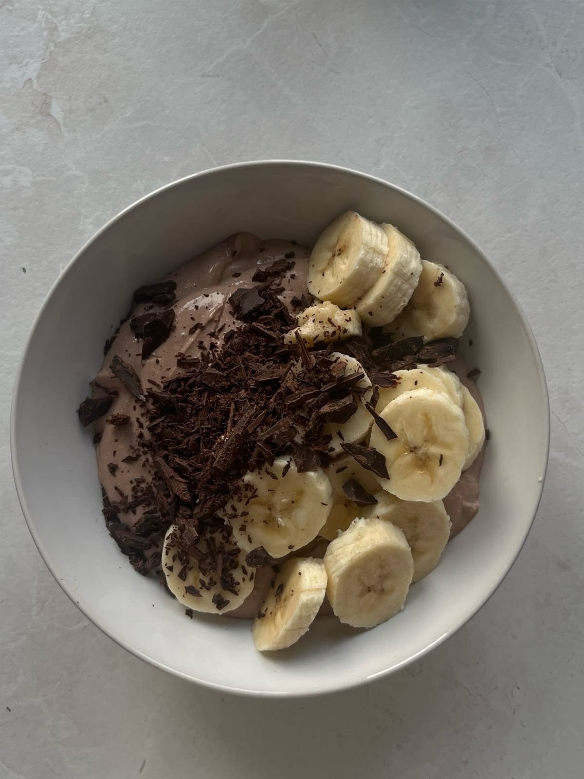 Purple smoothie bowl topped with fresh banana slices and dark chocolate shavings.
