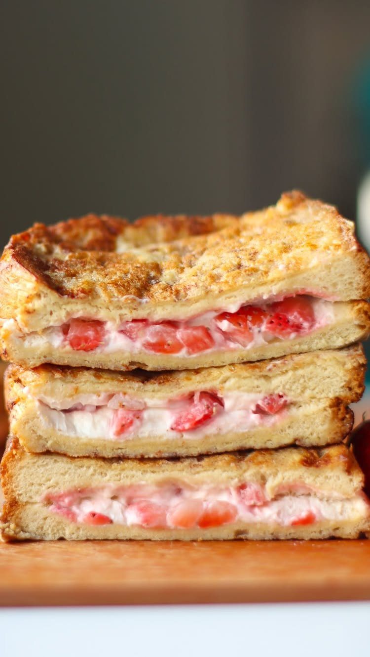 Stacked French toast slices filled with creamy strawberry cheesecake filling on a wooden board.