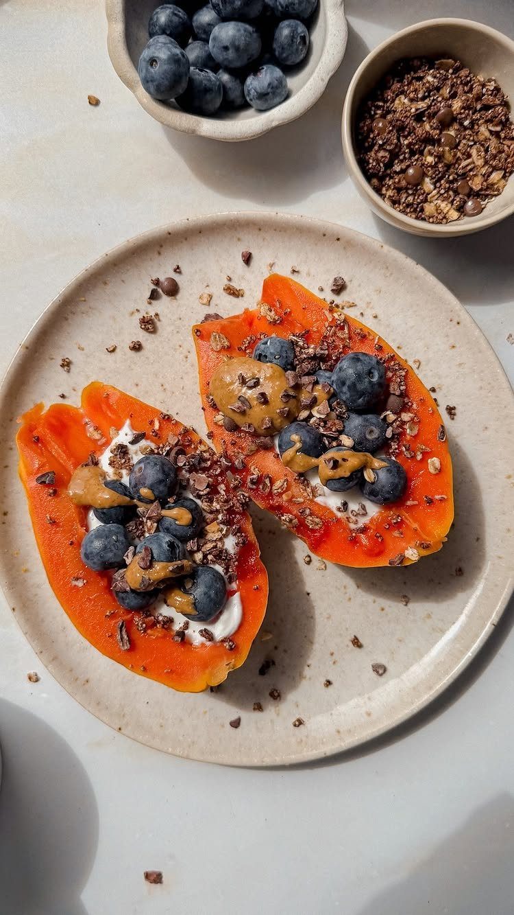 Papaya halves filled with yogurt, blueberries, and cocoa nibs on a beige plate.