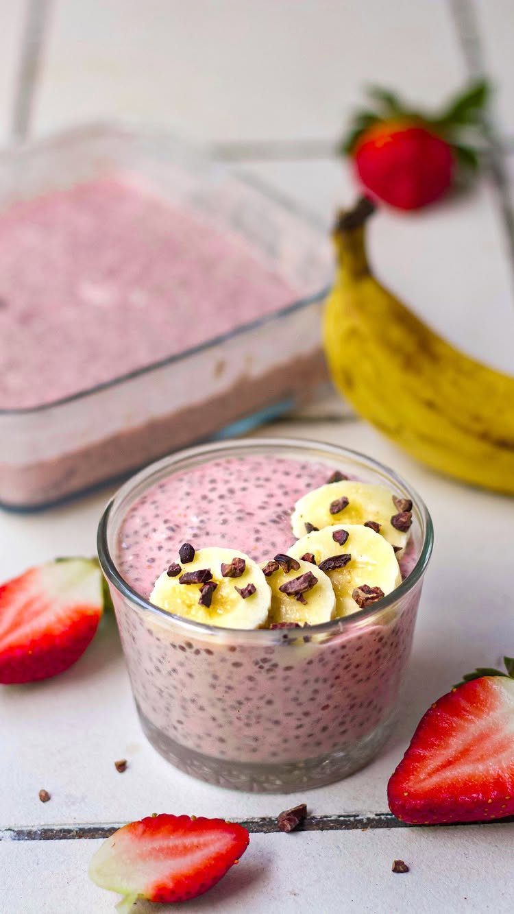 Pink berry chia pudding in a glass topped with banana slices and chocolate chips.