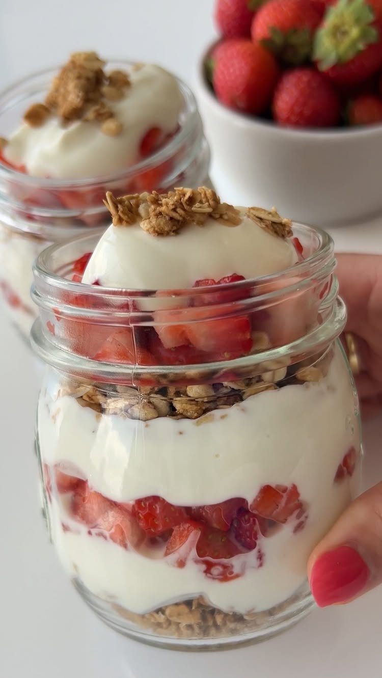 Yogurt parfaits with layers of strawberries and granola in glass jars.