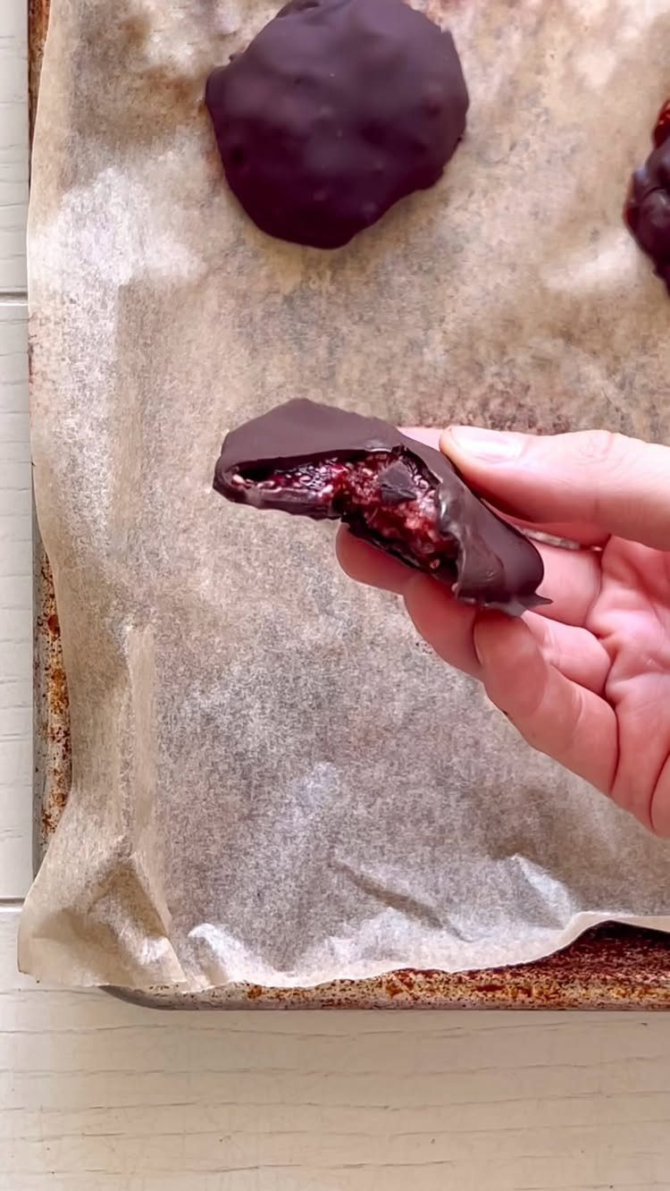 27 Easy Sweet Treats No Bake Ideas, From Fudge to Eton Mess 22 Chocolate-covered berry treat held by a hand over a parchment-lined baking sheet.