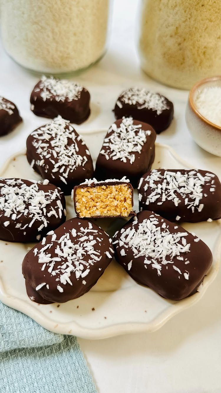 27 Easy Sweet Treats No Bake Ideas, From Fudge to Eton Mess 3 Chocolate coconut bars topped with shredded coconut on a white scalloped plate.