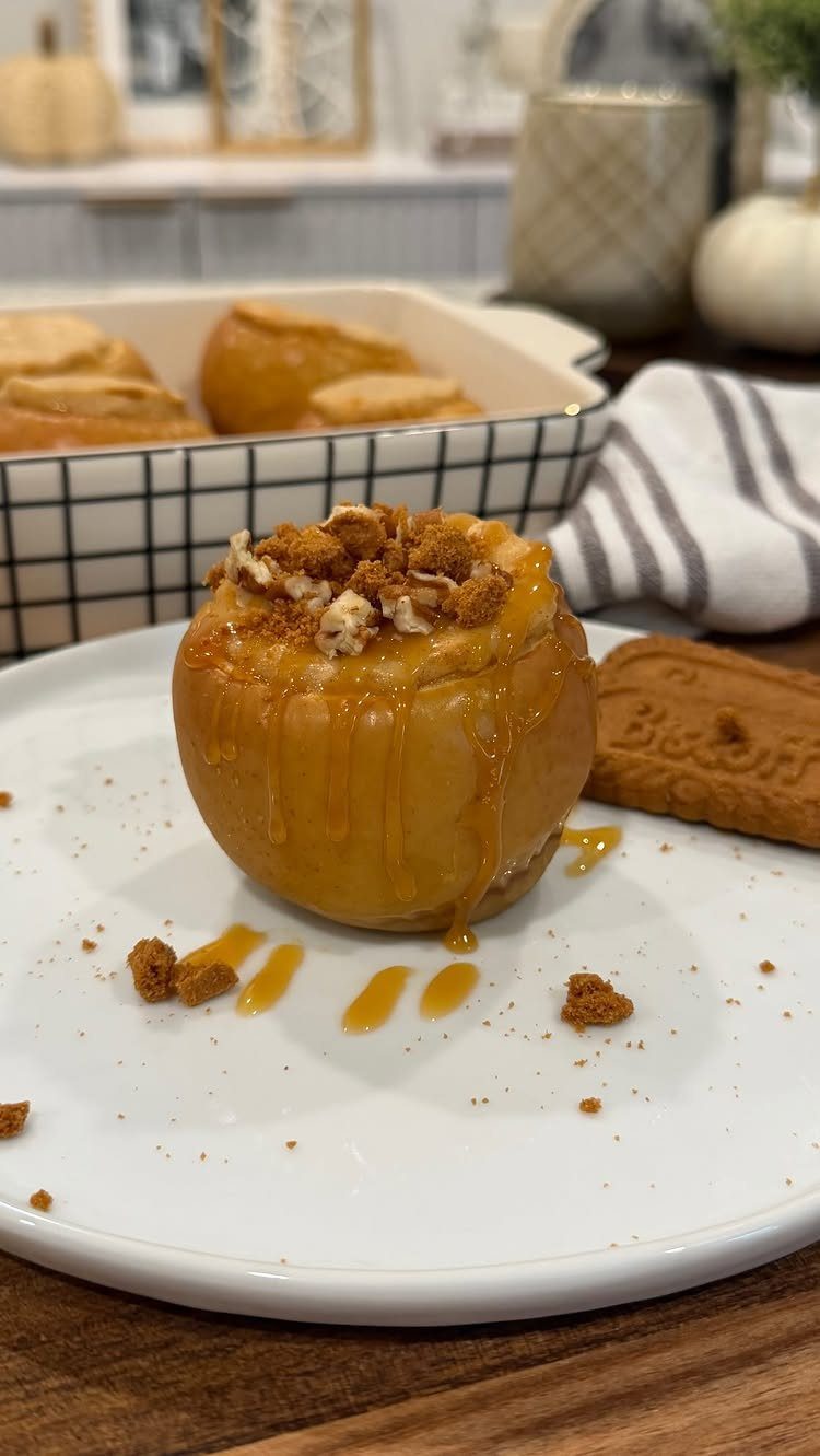 Baked apple with crumble topping and caramel drizzle on a white plate.