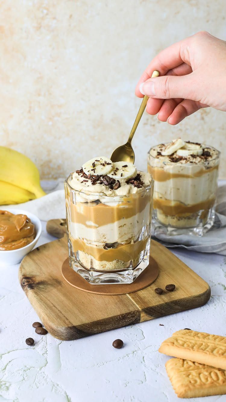 Layered banoffee pie dessert in glass jars topped with banana slices and chocolate.