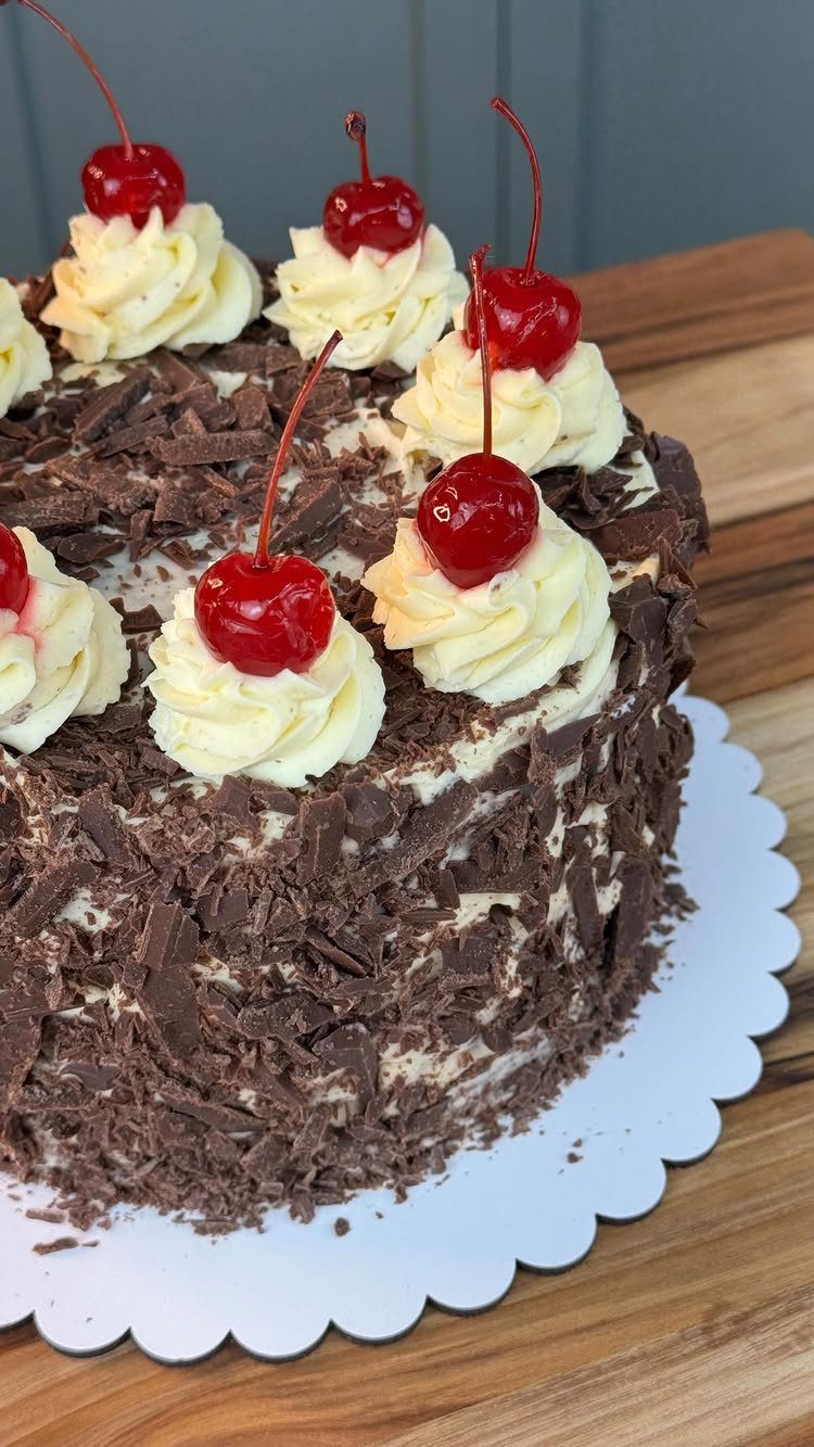Black Forest cake with chocolate shavings, whipped cream swirls, and red cherries on top.