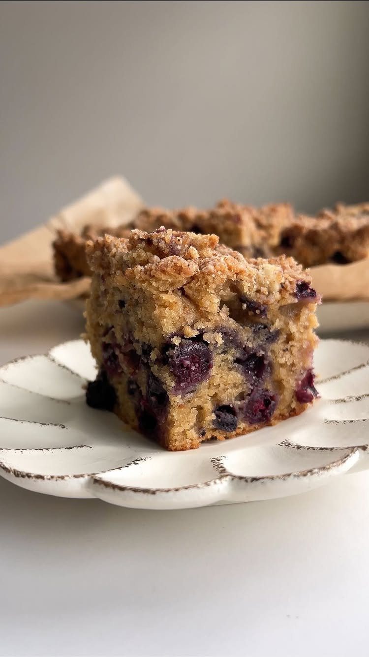 Blueberry coffee cake slice with crumb topping on a white scalloped plate.