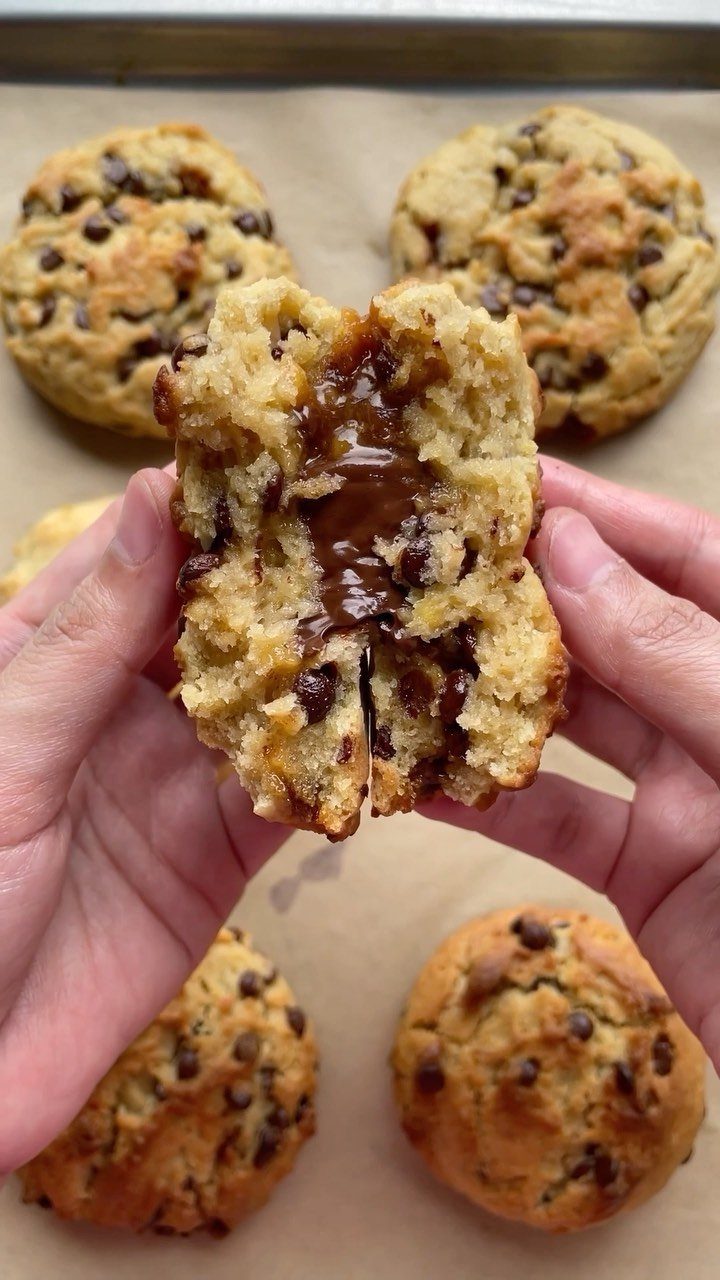 Chocolate chip cookies on parchment paper with one broken open showing melted chocolate.
