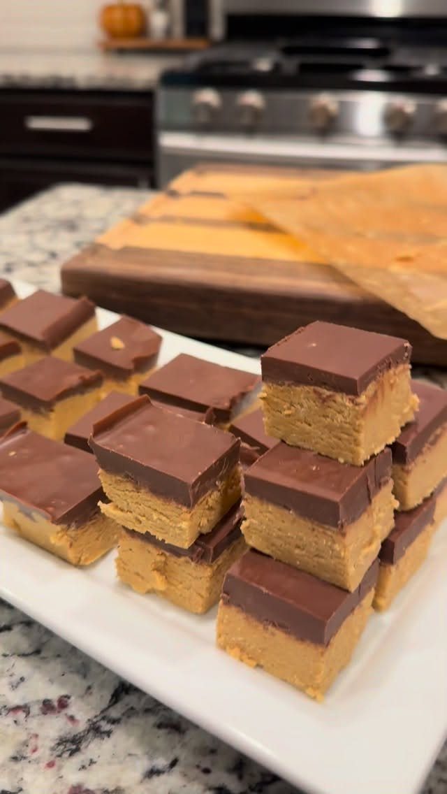 Chocolate peanut butter bars stacked on a white platter in a kitchen.