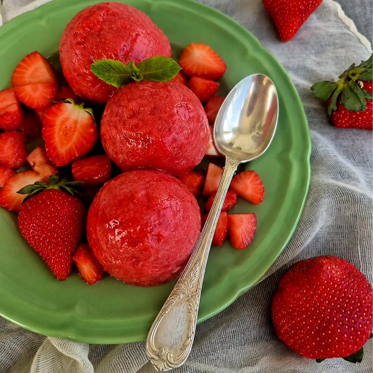 Strawberry sorbet scoops on a green plate with fresh strawberries and a silver spoon.