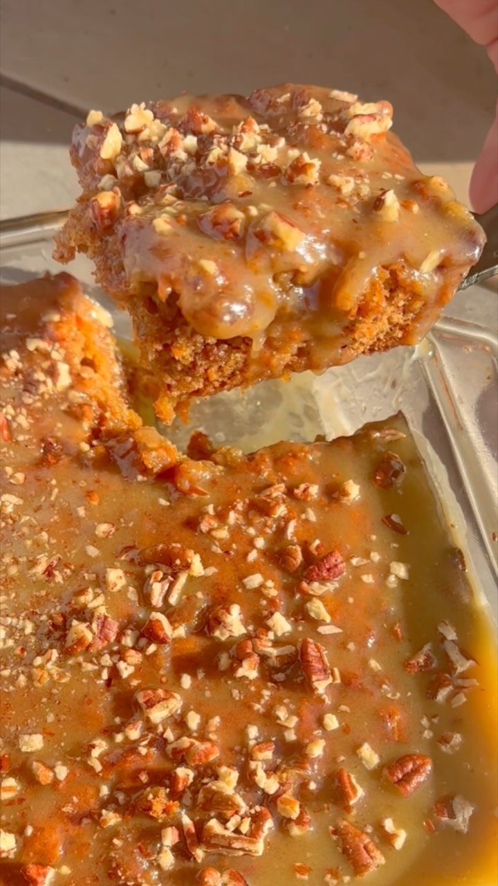 Caramel glazed cake with chopped nuts being lifted from a glass baking dish.