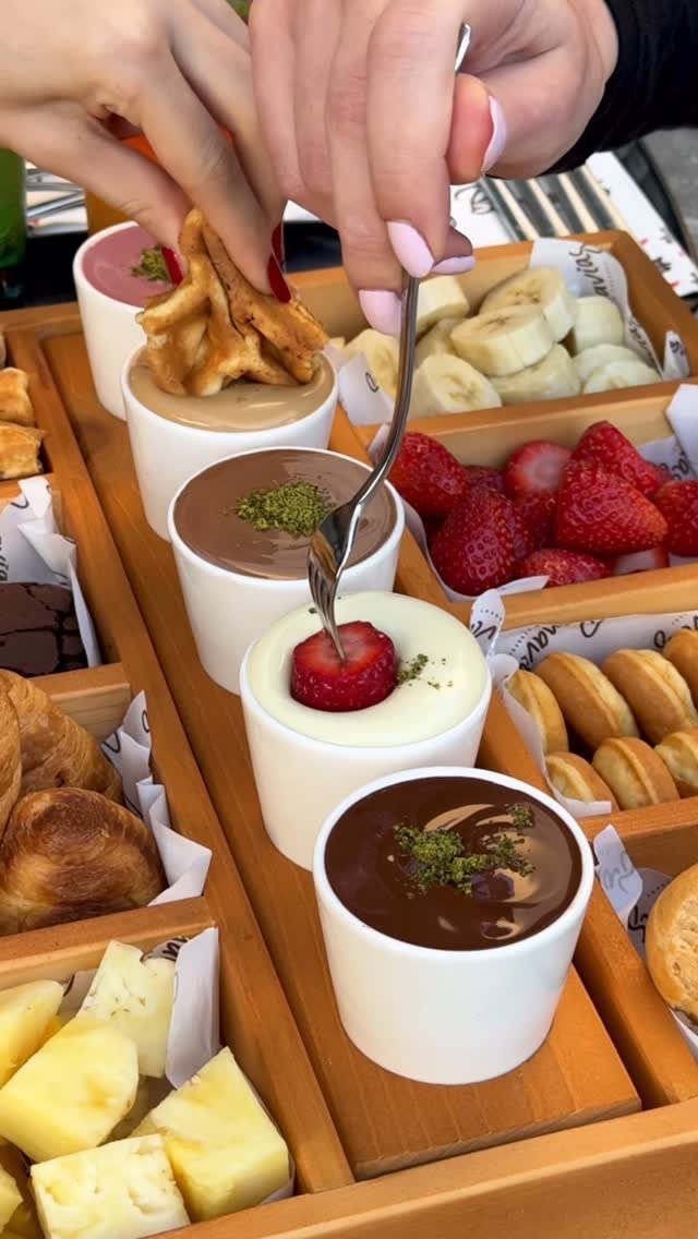 Fruit and pastry platter with chocolate dipping sauces and hands dipping food.
