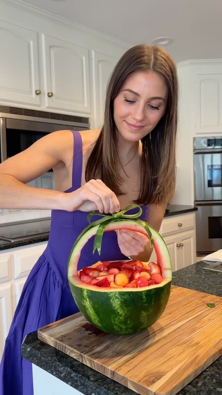 Watermelon carved into a basket filled with fruit, being decorated with a green ribbon.