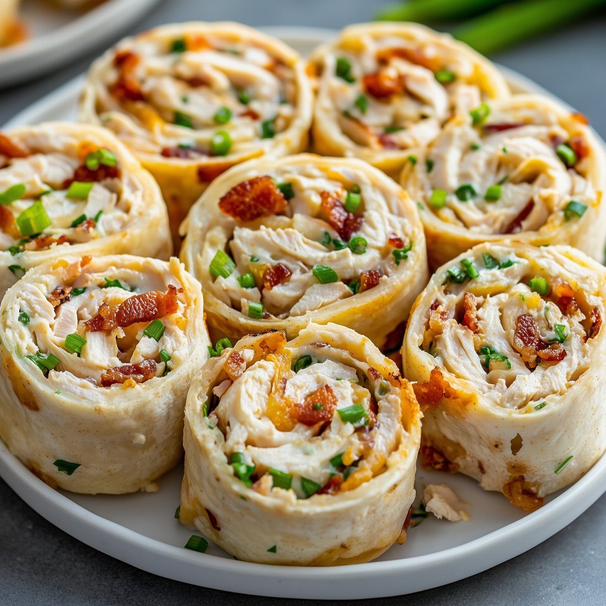 Chicken pinwheels with bacon and green onions on a white plate.