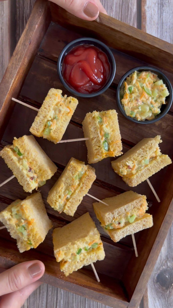 Small finger sandwiches with yellow filling on a wooden tray with dipping sauces.