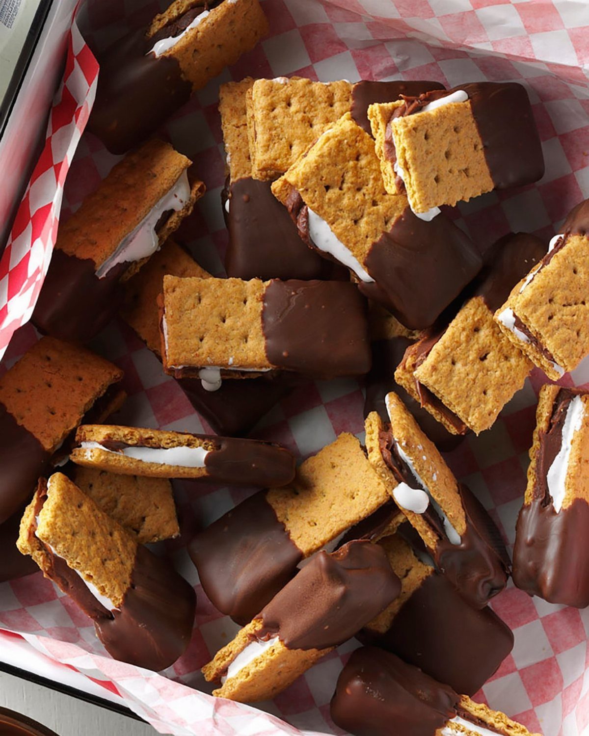 Chocolate-dipped s'mores with graham crackers and marshmallow in a checkered liner.