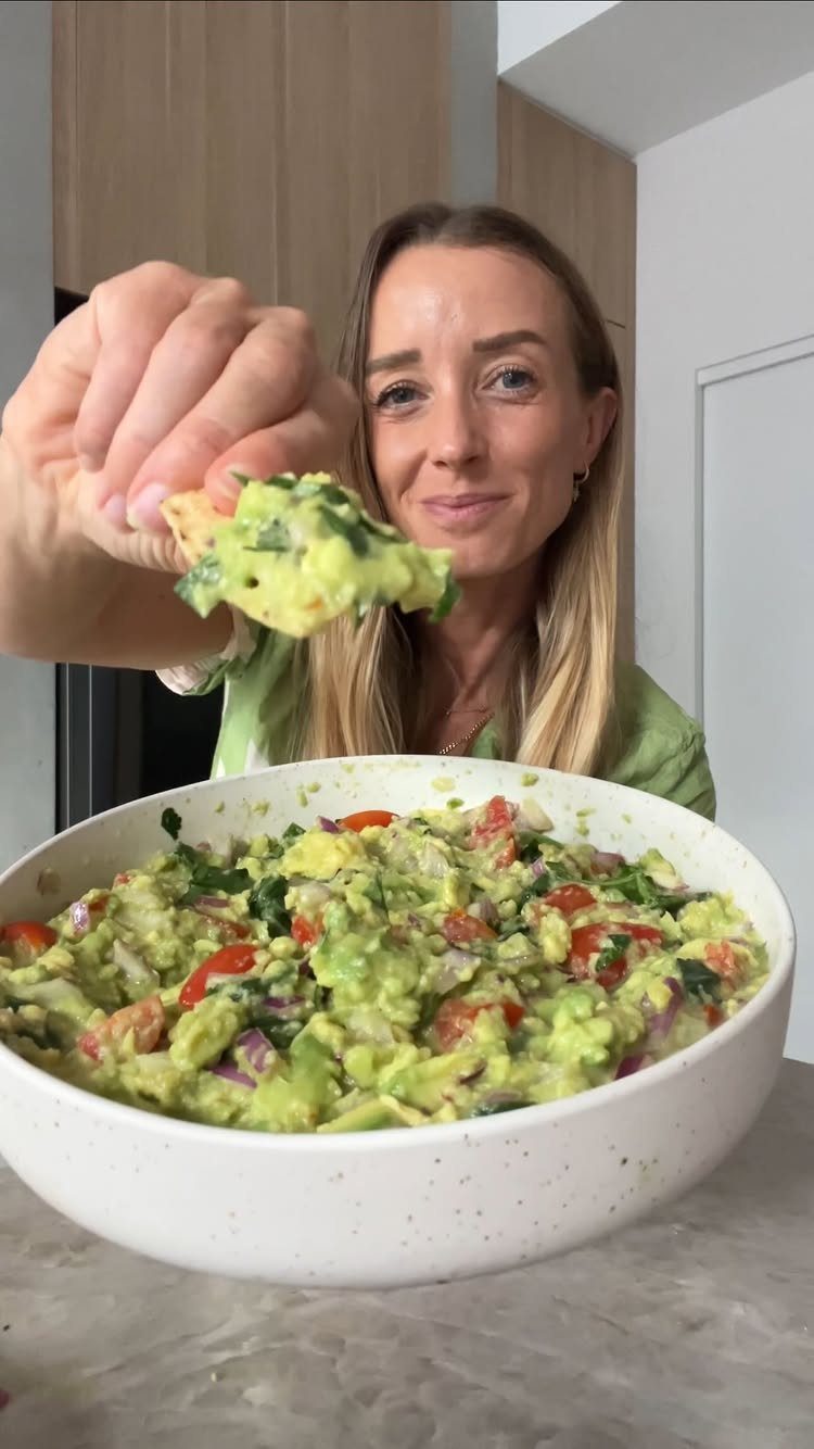 Guacamole with tomatoes and onions in a white bowl with a dipped chip.